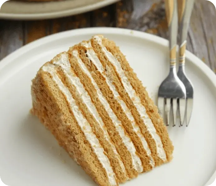 A single slice of Russian honey cake, created by Hive, elegantly presented on a plate. The cake is accompanied by two forks, ready to indulge in this scrumptious delight.